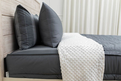 A side view of gray zipper bedding on a bed with the top unzipped halfway down and the comforter folded down.