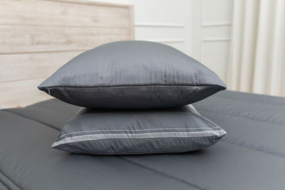 Gray pillows stacked on top of each other in the middle of a made bed with gray zipper bedding.  
