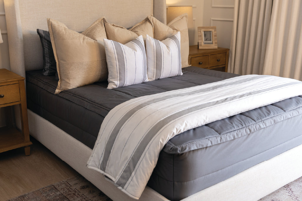 A bed made with gray zipper bedding and an assortment of neutral and striped throw pillows and blanket.