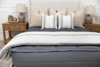 A bed made with gray zipper bedding and an assortment of neutral and striped throw pillows and blanket.