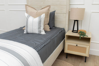 A twin bed made with gray zipper bedding and gray striped pillow and blanket.
