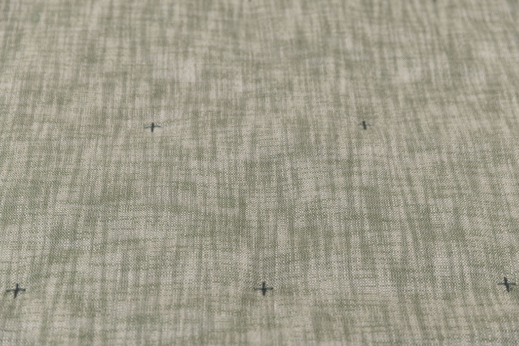 A close up view of a deep emerald green two-toned woven tweed exterior with embroidered cross-hatches of a zipper bedding.