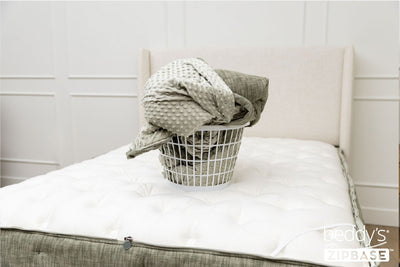 A bed made with just the fitted bedding base around the sides of the mattress, with the top comforter and ZipBase sheet in a basket on top of the bed.