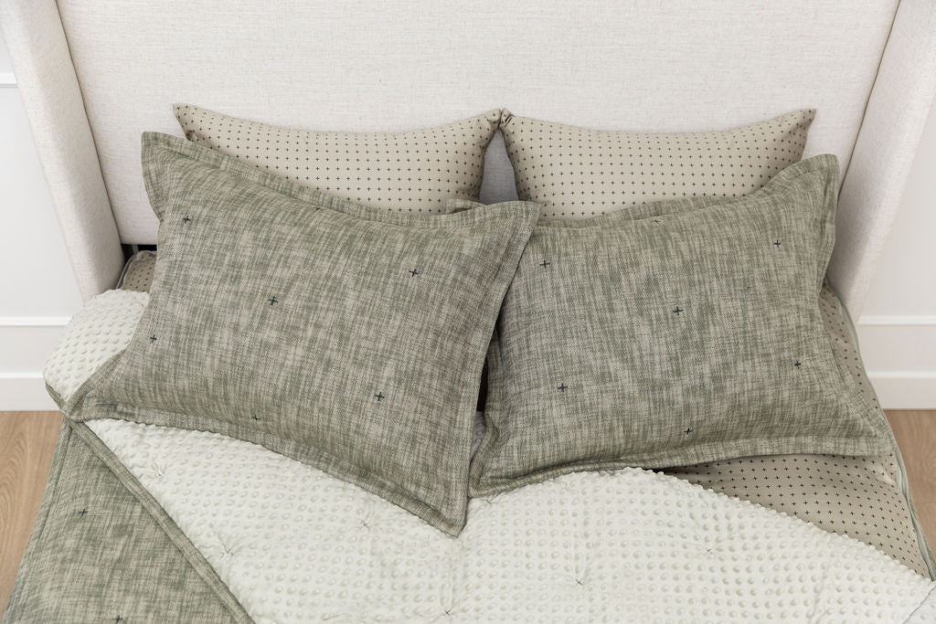 A bed made with deep emerald green zipper bedding with the comforter pulled back and pillows on top of the bed.
