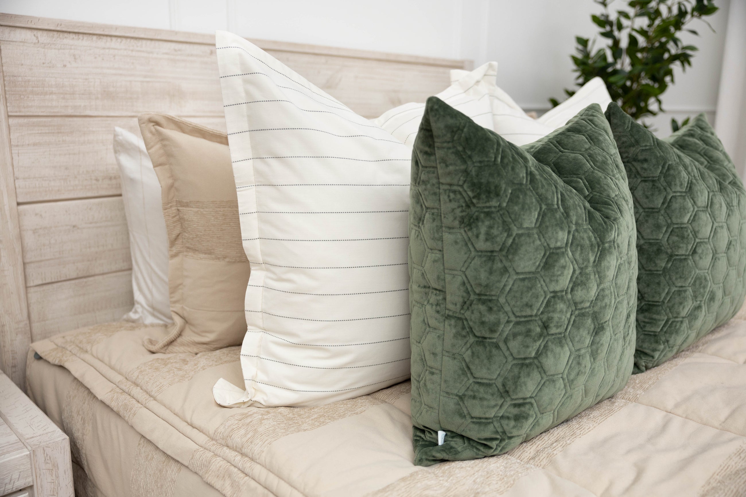 A close up side view of a bed made with tan zipper bedding and an assortment of white striped and green velvet pillows.
