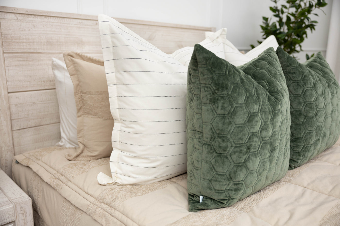 A close up side view of a bed made with tan zipper bedding and an assortment of white striped and green velvet pillows.