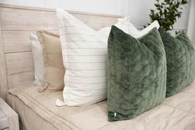 A close up side view of a bed made with tan zipper bedding and an assortment of white striped and green velvet pillows.