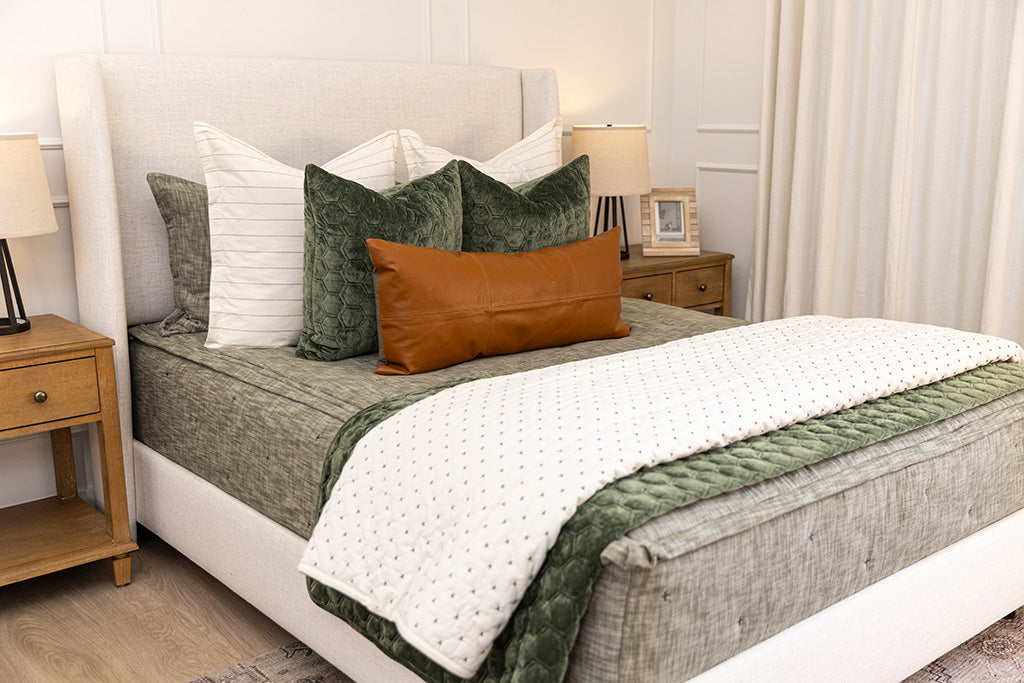 A queen bed made with deep emerald green zipper bedding and neutral and green throw pillows and blankets.