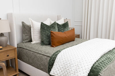 A queen bed made with deep emerald green zipper bedding and neutral and green throw pillows and blankets.