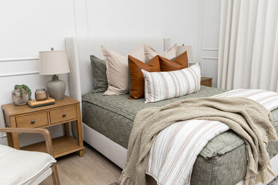A queen bed made with deep emerald green zipper bedding and neutral and tan striped pillows and blankets.