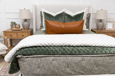 A bed made with deep emerald green zipper bedding and an assortment of neutral throw pillows and blankets.