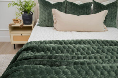 A close up of a bed made with cream embroidered zipper bedding and an assortment of neutral emerald velvet throw pillows and blanket.