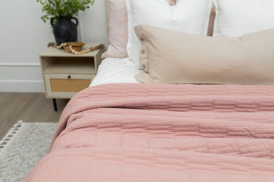 A close up of a bed made with white zipper bedding and neutral pillows as well as a pink quilted blanket.