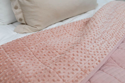 A close up of a bed made with white zipper bedding and neutral pillows with a pink blanket folded over to reveal it's minky interior.