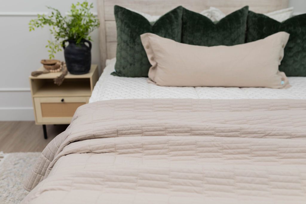 A bed made with cream embroidered zipper bedding and an assortment of neutral and velvet green throw pillows and blanket.