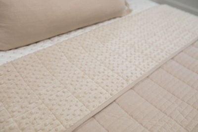 A close up view of a bed made with cream embroidered zipper bedding and a tan blanket folded over the bed revealing the minky interior.