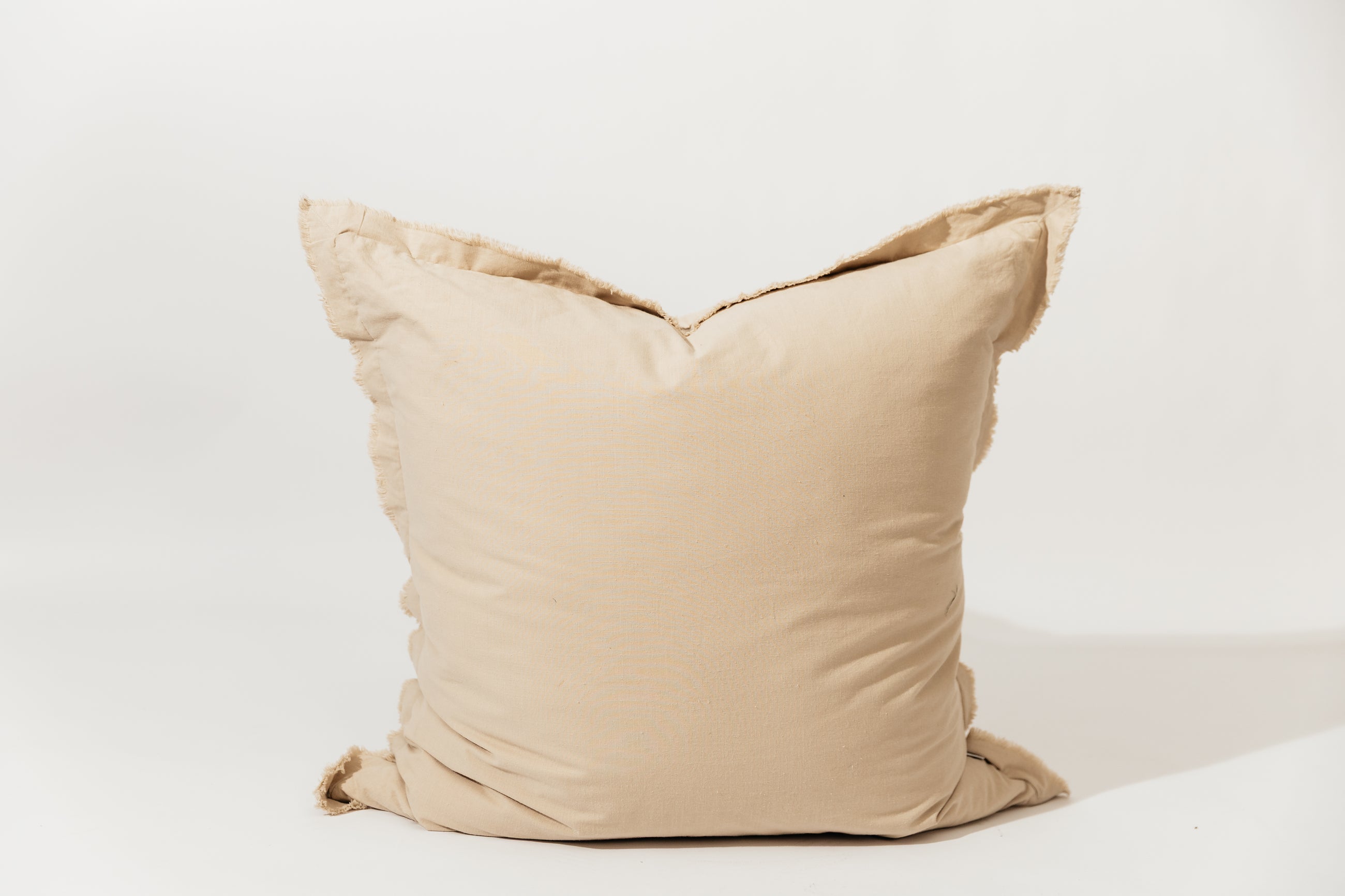 A neutral large tan pillow with frayed edges arranged on a white background.