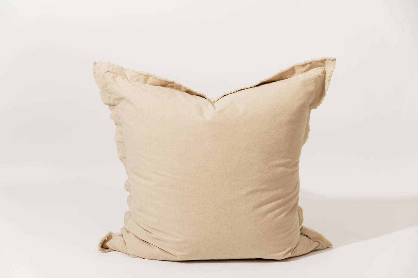 A neutral large tan pillow with frayed edges arranged on a white background.