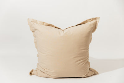 A neutral large tan pillow with frayed edges arranged on a white background.