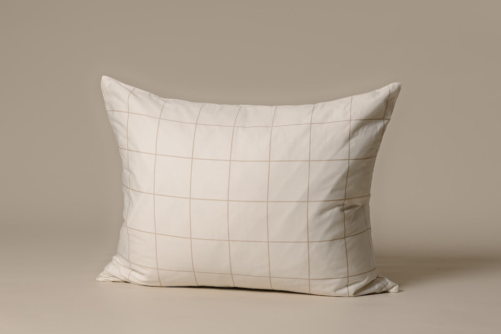 A cream and tan grid pillow on a cream backdrop.