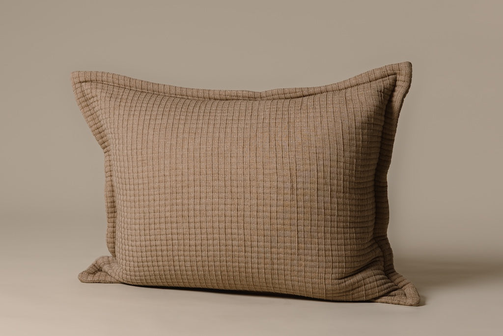 A light brown knitted sham on a cream backdrop.