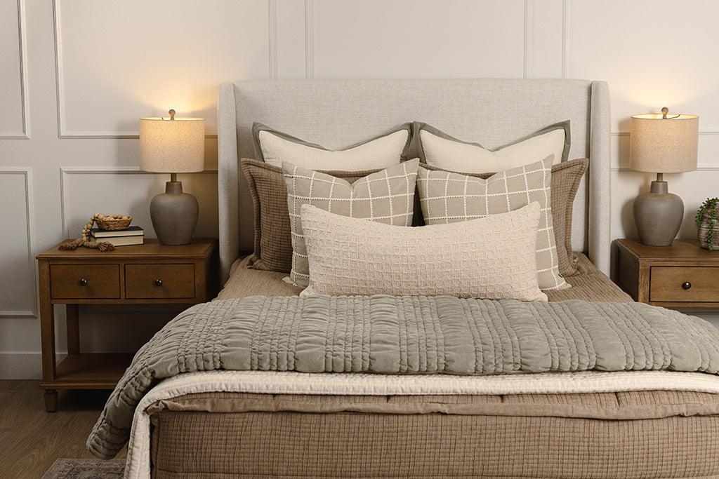 Tan woven quilted bedding with cream and green accessories. 