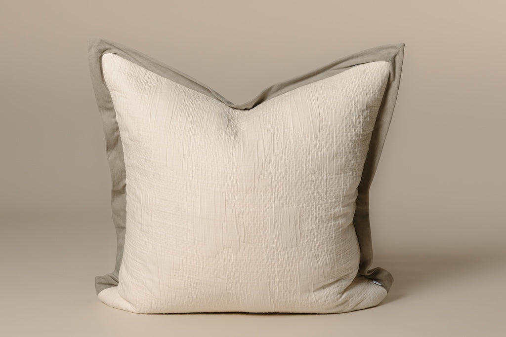 Cream knitted pillow with green velvet trim on cream background.