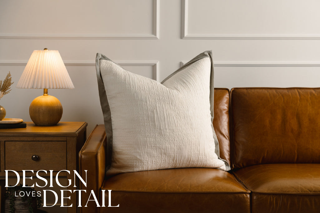 A cream textured and green velvet trim XL pillow on a leather couch.