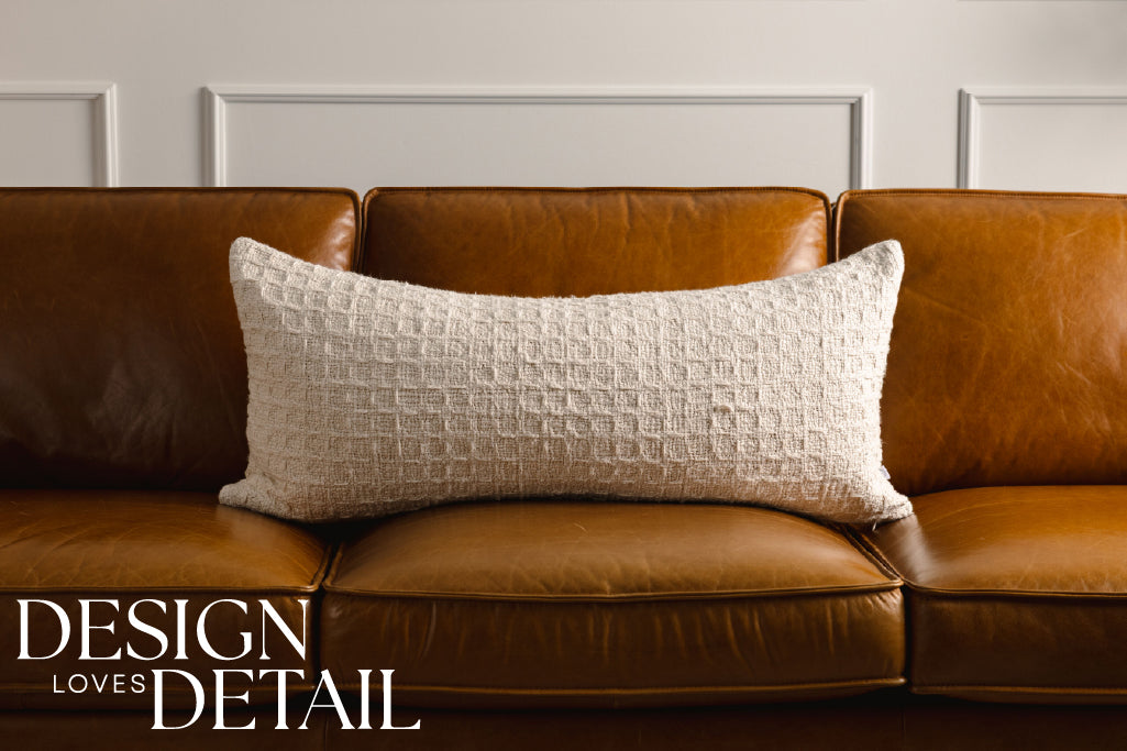 A cream woven XL lumbar pillow on a leather couch.