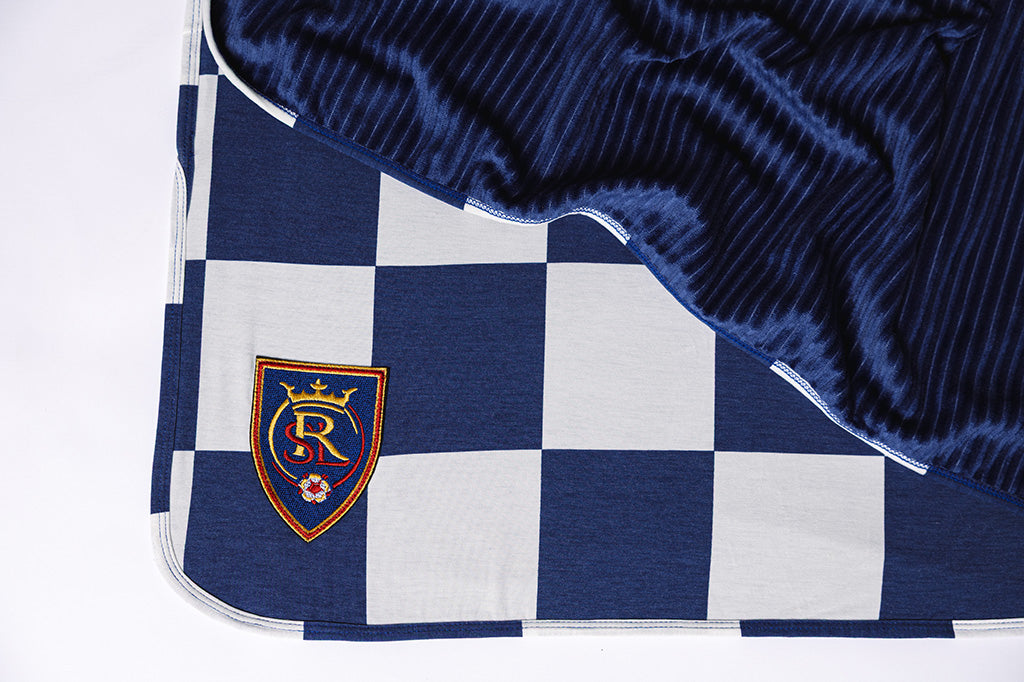 A blue and white checkered blanket with a RSL soccer logo on a white backdrop. 