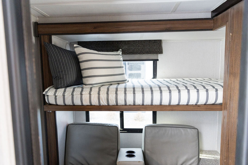 A brightly lit RV with a twin bunk bed made with striped black and white zipper bedding.