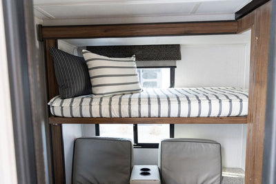 A brightly lit RV with a twin bunk bed made with striped black and white zipper bedding.