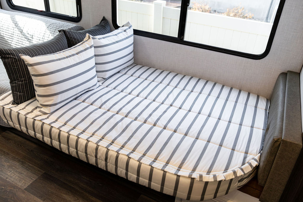 A rounded RV corner bed made with striped black and white zipper bedding.
