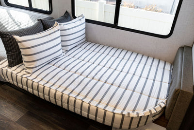 A rounded RV corner bed made with striped black and white zipper bedding.