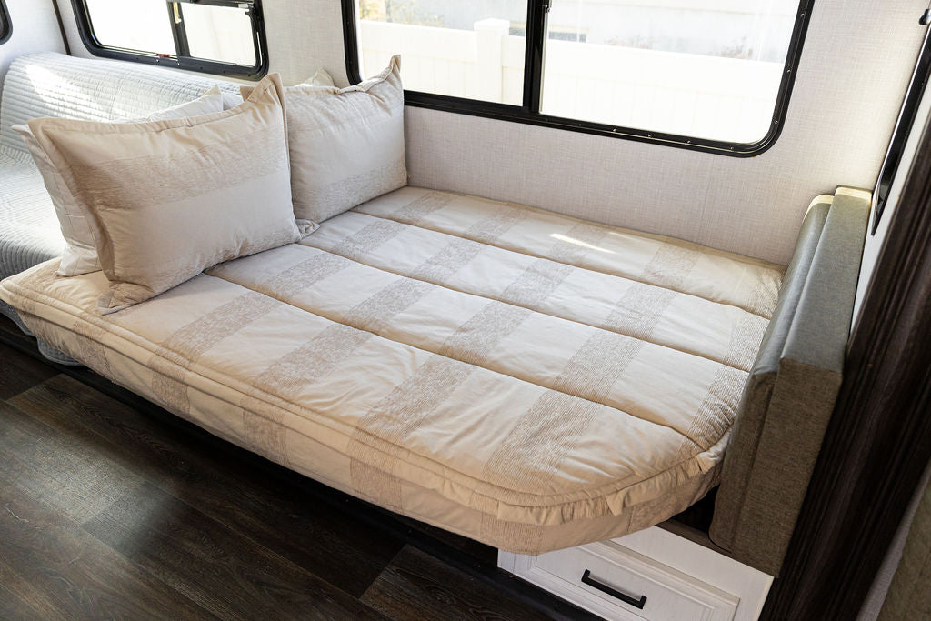 A rounded corner bed in an RV made with tan faded stripes zipper bedding and matching pillows.