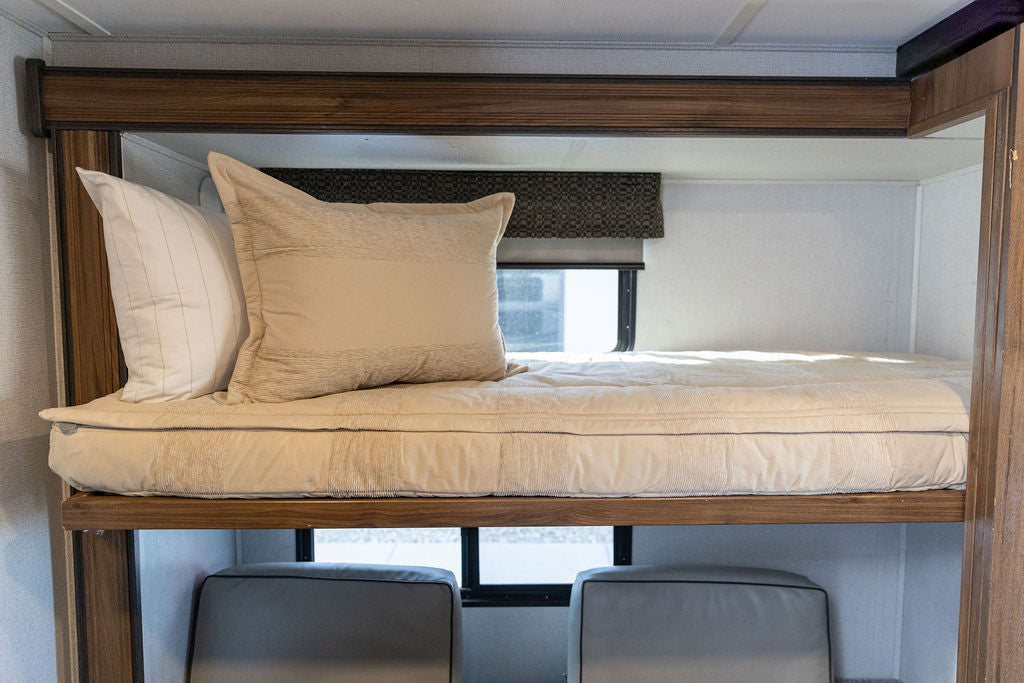 A bunk in an RV made with tan faded stripes zipper bedding and matching pillows.