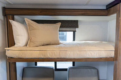A bunk in an RV made with tan faded stripes zipper bedding and matching pillows.