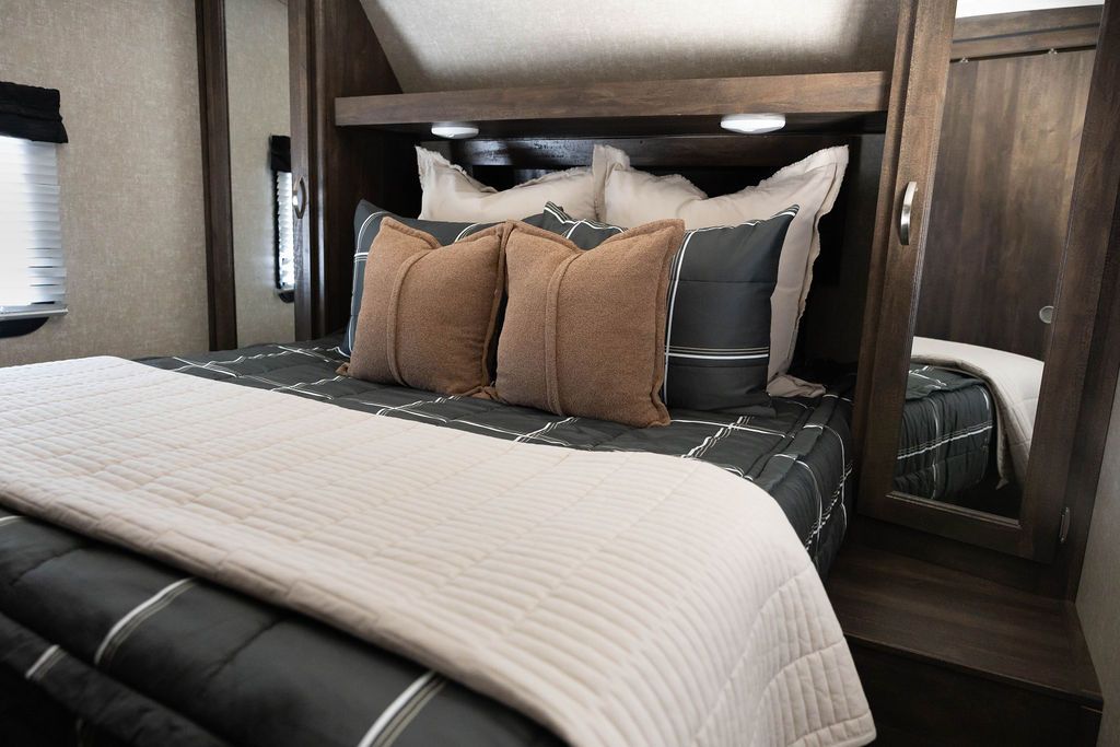 A queen bed in an RV made with black plaid zipper bedding and tan and brown throw pillows and a tan throw blanket