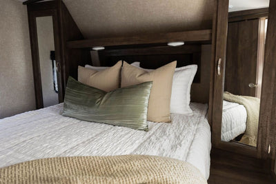 An RV bed made with seersucker white zipper bedding and neutral pillows.