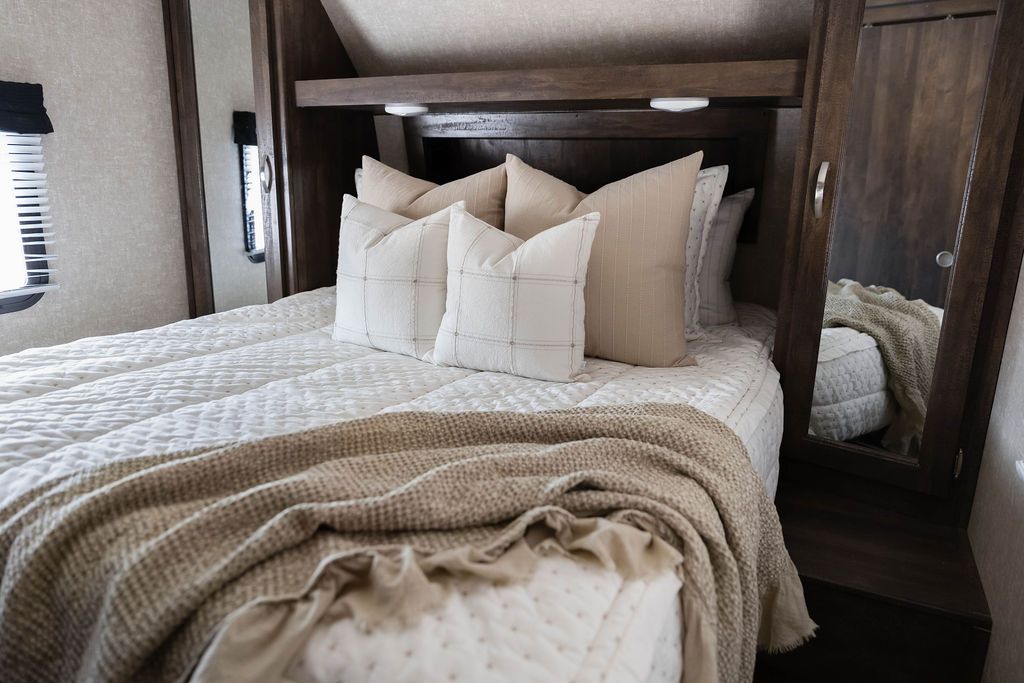 A bed in an RV made with cream embroidered zipper bedding and neutral pattern pillows and a throw blanket.