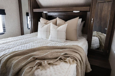 A bed in an RV made with cream embroidered zipper bedding and neutral pattern pillows and a throw blanket.