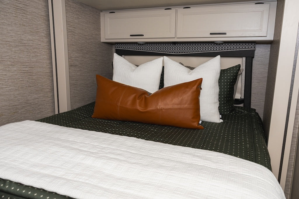 A bed made in an RV with green zipper bedding and an assortment of tan and white pillows and blankets.