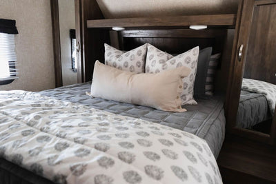 A Queen bed in an RV made with gray zipper bedding and neutral floral bedding accessories.