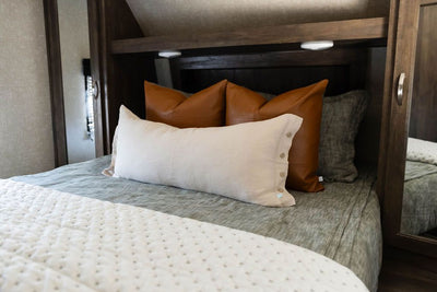 A bed in an RV made with deep emerald green zipper bedding and neutral and leather pillows and blanket.
