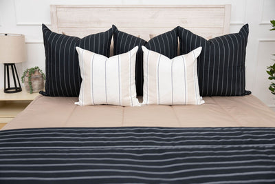 A bed made with tan zipper bedding and black and white and neutral bedding accessories
