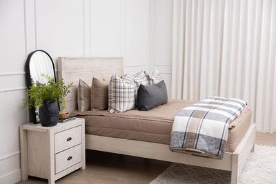 A bed made with tan zipper bedding and an assortment of neutral plaid pattern pillows and blanket.