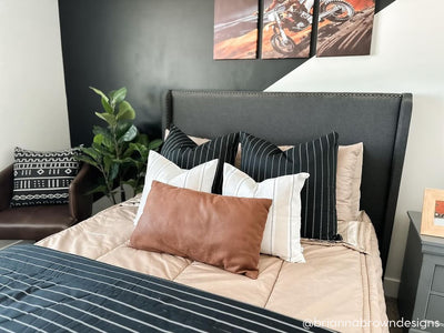 A close up view of a bed made with tan zipper bedding and an assortment of neutral pillows and blanket.