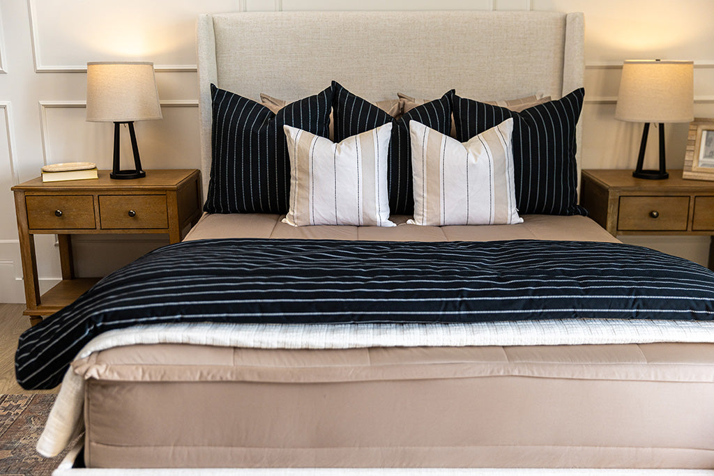 A bed made with tan zipper bedding and an assortment of neutral and black pillows and blanket.
