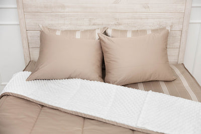 A bed made with tan zipper bedding with the comforter pulled back showing minky interior lining and pillows on top of the bed.