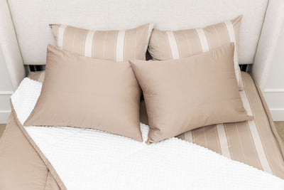 A bed made with tan zipper bedding with the comforter pulled back and pillows on top of the bed.